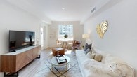 This single-floor residence presents a cohesive, modern design characterized by a neutral palette of whites and warm earth tones throughout. The open living area is anchored by light wood-style flooring, large windows that draw in abundant natural light, and views of the surrounding neighborhood. The space comfortably accommodates both a seating area and a dining nook, creating a versatile, welcoming layout.

The kitchen is outfitted with flat-front wood cabinetry, granite-style countertops, stainless steel appliances including a gas range and French door refrigerator, and a deep undermount sink — offering both functionality and a clean aesthetic.

The primary bedroom features a tray ceiling, plush carpeting, and a window overlooking the outdoors. An en-suite bathroom connects via a hallway and includes a double-sink vanity with light wood cabinetry, a white quartz countertop, and a large mirror.

A second bedroom maintains the same soft, carpeted warmth with a bright window and direct bathroom access through a dedicated hallway. Each bathroom echoes the same refined, contemporary style with sleek light wood vanities and clean white finishes throughout.