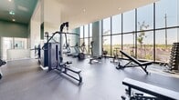 Located at 300 Avenue de l'Équinoxe in Brossard, Quebec, this fitness facility offers a thoughtfully designed space that combines functionality with a clean, modern aesthetic. The gym is organized across a single floor and comprises a main exercise room and a bathroom.

The exercise room is the heart of the facility, bathed in abundant natural light streaming through expansive floor-to-ceiling windows that frame open outdoor views. The main workout area features durable rubber flooring and is outfitted with a comprehensive selection of equipment, including treadmills, stationary bikes, rowing machines, cable machines, pull-up stations, and weight benches. Full-length mirrors line the walls, visually expanding the space and allowing members to monitor their form. Bold black-and-white athletic photography adorns one wall, adding energy and motivation to the environment. A French-language motivational inscription — "chaque EFFORT t'amènera plus près de ton OBJECTIF" — reinforces the facility's encouraging atmosphere.

A separate, serene area with light hardwood flooring, soaring ceilings, and tall windows serves as a dedicated stretching or yoga zone. This bright, minimalist space features floor-level decorative white pebble beds framing a large mirror wall, lending a tranquil, spa-like ambiance. A lush potted plant and subtle décor complete this peaceful retreat within the facility.