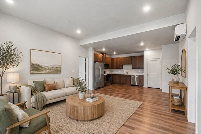 Chic open-concept living area featuring modern kitchen with dark wood cabinets, plank flooring, and stainless steel appliances. - Lofts at Garden District