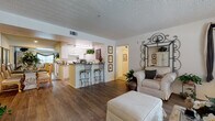 This single-floor residence offers a thoughtfully designed open-concept layout that seamlessly connects the living, dining, and kitchen areas. The living room features warm hardwood-style flooring, a textured ceiling, and large windows dressed with elegant draping, allowing generous natural light to filter in. A sliding glass door opens to a private patio, further enhancing the sense of openness. An ornate iron mirror and framed wall art add character to the space.

The kitchen is equipped with white cabinetry, white appliances including a range and refrigerator, and granite-style countertops. A peninsula with bar seating provides a casual dining option, while a separate dining area accommodates formal meals. The kitchen opens directly to the living and dining spaces, promoting a connected and social atmosphere.

The primary bedroom features plush carpeting, a ceiling fan, natural light from a window with blinds, and ample space for a full furniture suite. It connects to a generous walk-in closet with wire shelving. A second bedroom also offers carpeted flooring and a sliding closet. The bathroom includes a vanity with stone-style countertops, a tub-shower combination, and hardwood-style flooring, completing this comfortable and functional residence.
