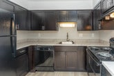 Located at 17600 W 13 Mile Rd in Beverly Hills, Michigan, this single-floor unit offers a thoughtfully designed layout with a blend of modern finishes and comfortable living spaces. The kitchen is a standout feature, showcasing sleek dark cabinetry with brushed nickel hardware, light marble-style countertops, and black appliances including a dishwasher, range, and overhead ventilation. Light wood-style flooring grounds the kitchen, creating a striking contrast against the dark cabinetry. The open layout connects the kitchen to the main living area, which is finished with plush wall-to-wall carpeting and neutral-toned walls that maximize brightness. A large sliding glass door in the living room floods the space with natural light and provides outdoor access. A hallway with warm pendant lighting and built-in shelving leads to the private areas of the unit, including a generously sized bedroom with soft carpet flooring, a window with natural light, and access to a dedicated walk-in closet complete with built-in shelving and hanging rods. The full bathroom features wood-style flooring, a dark vanity with marble-style countertop, and a full tub and shower combination with classic white tile surround.