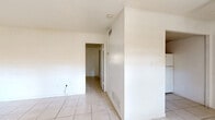 Located at 926 East Fort King Street in Ocala, Florida, this single-story, one-bedroom, one-bathroom unit offers a straightforward and functional layout. Light-colored ceramic tile flooring runs consistently throughout the entire space, creating a cohesive and easy-to-maintain interior.

The main living area combines the living room, dining room, and kitchen into one open-concept space. The living room is bright and airy, featuring two front-facing windows that allow natural light to fill the room, complemented by a ceiling fan overhead. The kitchen is positioned at the rear of this open area and is equipped with warm-toned wooden cabinetry — both upper and lower — a countertop with an integrated sink, and a full-size refrigerator.

A hallway connects the main living area to the private spaces, including the spacious bedroom, which features a window with an outdoor view and two closets providing ample storage. The bathroom includes a vanity with a sink and wood cabinetry, a wall-mounted mirror, a toilet, and a shower-tub combination enclosed by a curtain. Classic octagonal tile flooring adds a distinctive touch to the bathroom floor.

Overall, the unit presents a clean, minimalist interior with white walls throughout, offering a blank canvas ready for personalization.