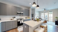 This single-floor residence showcases a thoughtfully designed open-concept layout with a cohesive modern aesthetic throughout. The kitchen serves as a centerpiece, featuring floor-to-ceiling gray shaker-style cabinetry, a herringbone-patterned tile backsplash, and white quartz countertops. A spacious center island with an undermount sink and bar seating provides additional prep and dining space, while stainless steel appliances—including a gas range, built-in microwave, and French door refrigerator—complete the well-equipped cooking area. Stylish matte black pendant lights illuminate the island.

The living area flows naturally from the kitchen and is anchored by light hardwood flooring that extends throughout the unit. Large glass doors lead to a private balcony offering views of the surrounding modern complex and palm trees below. A ceiling fan, built-in shelving nook, and neutral wall tones create a comfortable, airy atmosphere.

The bedrooms are bright and restful, each benefiting from large windows with roller shades that frame views of the exterior courtyard. Warm hardwood flooring, clean lines, and ceiling fans contribute to a calm, functional environment. Overall, the space presents a contemporary, well-appointed interior with consistent finishes and an emphasis on natural light.