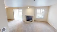 Located at 5617 111th St E, Unit 201, in Puyallup, Washington, this single-floor unit offers a thoughtfully designed layout with comfortable finishes throughout. The living room serves as the focal point of the home, featuring a tile-surround fireplace with a clean white mantle and soaring ceilings that lend an open, airy feel. Soft wall-to-wall carpeting extends throughout the living and bedroom areas, adding warmth underfoot. Large windows and a sliding glass door allow natural light to fill the space while providing views of the surrounding exterior. The kitchen is equipped with light maple cabinetry, granite-style countertops, and a stainless steel range, offering both functionality and a clean aesthetic. The bedrooms are generously proportioned, each featuring carpeted floors, natural light from windows, and baseboard heating. At least one bedroom includes a closet with shelving and a hanging rod, providing practical storage. The neutral color palette of warm beige and white tones is consistent throughout the unit, creating a cohesive and inviting atmosphere. The overall layout, as visible from the dollhouse view, flows efficiently between the living, kitchen, and bedroom areas, making this a comfortable and functional residence in Puyallup.