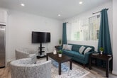 Located at 14815 Pioneer Blvd in Norwalk, California, this two-story residence offers a thoughtfully designed interior with a clean, contemporary aesthetic throughout. The color palette is light and neutral, accented by teal and aqua tones that carry cohesively from room to room.

The kitchen is a standout feature, outfitted with crisp white shaker-style cabinetry, granite-look countertops, and a full suite of stainless steel appliances including a gas range, built-in microwave, dishwasher, and refrigerator. Light wood-style flooring runs throughout the main living areas, enhancing the bright, open feel of the space.

The living room offers a welcoming layout with recessed lighting, large windows that invite natural light, and views of the surrounding neighborhood. A dining area sits adjacent, creating a functional flow for everyday living.

The bedrooms are carpeted and well-proportioned, each featuring windows with teal drape accents. One bedroom includes a mirrored sliding closet, while another benefits from outdoor views and ample natural light.

Two bathrooms serve the home, one featuring a tub-shower combination with stone-look countertops and white cabinetry, and the other a walk-in shower stall, both finished with light wood-style flooring and modern fixtures.