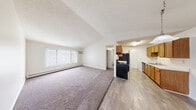 This single-floor, 2-bedroom, 2-bathroom residence offers a functional and comfortable layout designed for everyday living. The open-concept living room and kitchen area forms the heart of the home, with plush carpeting underfoot and a large window fitted with vertical blinds that fills the space with natural light. A wood-mantled fireplace with a classic surround serves as a charming focal point, complemented by a hanging pendant light overhead. The kitchen is adjacent to the living area and features warm wood cabinetry, a black refrigerator and range, a dishwasher, and light wood-tone flooring that extends through the dining space.

A hallway connects the living areas to the two bedrooms, each finished with soft carpet, baseboard heating, and ceiling fans with lighting. The spacious primary bedroom includes a walk-in closet outfitted with dual hanging rods and shelving, offering ample storage. A second closet provides additional organization. Both bathrooms feature tub-shower combinations, wood-tone vanities, and clean, neutral finishes.

The dedicated laundry room houses a full-size washer and dryer, adding everyday convenience. Textured ceilings are present throughout, and baseboard heating ensures year-round comfort in this practical and well-organized residence.
