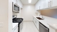 Located at 5409 Carlton Way in the heart of Los Angeles, CA 90027, this single-floor unit offers a clean, modern aesthetic throughout its well-appointed layout. Rich, hardwood-style plank flooring flows seamlessly across the living and dining areas, lending warmth and visual continuity to the space. The living room is bright and open, anchored by a large sliding glass door framed by dark grommet curtains that invite natural light and provide views of lush greenery outside. The galley-style kitchen is thoughtfully designed with crisp white shaker cabinetry, sleek quartz countertops, light tile flooring, and a full suite of stainless steel appliances including a gas range, over-the-range microwave, and dishwasher. A pass-through peninsula connects the kitchen to the main living area, creating an open, communicative flow ideal for everyday living. A hallway leads to the bedroom and bathroom, maintaining a sense of privacy. The bathroom features a full tub and shower combination with stainless steel safety grab bars and clean white finishes throughout. Neutral wall tones and consistent ceiling-mounted lighting fixtures give the entire unit a cohesive, move-in-ready appearance. The space strikes a balance between functional design and comfortable living in a desirable Los Angeles neighborhood.