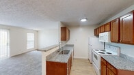 Located at 5701 Ebner Cir in Dublin, Ohio, this single-floor, two-bedroom, one-bathroom residence offers a well-organized and functional layout spanning a comfortable footprint. The kitchen is a standout feature, showcasing warm medium-toned wood cabinetry, granite-look countertops, and light hardwood-style flooring. A peninsula with a stainless steel sink opens directly to the living area, creating a connected and practical space. White appliances, including a refrigerator, electric range, and built-in microwave, complement the classic design. A pendant light fixture adds a subtle decorative touch above the transition to the carpeted living area. Both bedrooms are generously proportioned, finished with plush carpet flooring and neutral walls that allow for flexible furnishing. Each room benefits from natural light through vertical-blind-covered windows that offer outdoor views. The primary bedroom includes a dedicated closet with built-in shelving and hanging rods, while an additional closet provides further storage. The bathroom is equipped with a full walk-in shower enclosed by a sliding glass door with chrome hardware. Textured ceilings are consistent throughout, lending a traditional residential character to the entire space.