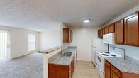 Located at 5701 Ebner Cir in Dublin, Ohio, this single-floor, two-bedroom, one-bathroom residence offers a well-organized and functional layout spanning a comfortable footprint. The kitchen is a standout feature, showcasing warm medium-toned wood cabinetry, granite-look countertops, and light hardwood-style flooring. A peninsula with a stainless steel sink opens directly to the living area, creating a connected and practical space. White appliances, including a refrigerator, electric range, and built-in microwave, complement the classic design. A pendant light fixture adds a subtle decorative touch above the transition to the carpeted living area. Both bedrooms are generously proportioned, finished with plush carpet flooring and neutral walls that allow for flexible furnishing. Each room benefits from natural light through vertical-blind-covered windows that offer outdoor views. The primary bedroom includes a dedicated closet with built-in shelving and hanging rods, while an additional closet provides further storage. The bathroom is equipped with a full walk-in shower enclosed by a sliding glass door with chrome hardware. Textured ceilings are consistent throughout, lending a traditional residential character to the entire space.
