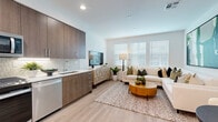 This contemporary two-story home in Chula Vista's Otay Ranch community offers a well-designed layout across two floors. The entry level features a versatile flex space bathed in natural light from large windows with sheer drapery, ideal for a home office or den, alongside convenient access to the main staircase. Light-toned hardwood-style flooring flows seamlessly throughout both levels, enhancing the home's bright, modern aesthetic. The upper floor hosts an open-concept kitchen and living area. The kitchen is outfitted with rich wood-toned cabinetry, a geometric tile backsplash, stainless steel appliances including a gas range, dishwasher, and side-by-side refrigerator, plus a crisp white countertop and undermount sink. The adjoining living room is generously proportioned with a wide window arrangement that fills the space with natural light. The bedroom is a serene retreat, featuring a textured accent wall, large window, and ample space for a full furniture arrangement. The full bathroom offers a clean, modern vanity with quartz countertop, wood cabinetry, and a walk-in shower. Recessed lighting and clean white walls throughout contribute to an overall atmosphere that is polished, airy, and move-in ready.