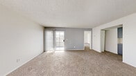 Located at 3955 E Charleston Blvd in Las Vegas, Nevada, this one-bedroom, one-bathroom unit offers a practical and well-organized single-floor layout. The living room serves as the centerpiece of the home, featuring wall-to-wall carpeting, neutral gray accent walls, and a textured ceiling. A sliding glass door fitted with vertical blinds opens to a private balcony, allowing natural light to fill the space and providing outdoor views of the surrounding area. The kitchen is efficiently designed in a U-shaped configuration, featuring gray cabinetry, speckled gray countertops, a double sink, white appliances including a refrigerator and electric range, and durable wood-look flooring. A breakfast bar peninsula adds additional counter space and a casual dining option. The bedroom is a generously sized, carpeted retreat with a window that brings in natural light, a closet, and a textured ceiling. A hallway connects the main living areas to the bedroom and bathroom, which includes a full tub-shower combination with white tile surround. The entry area features a paneled front door and a side window. Overall, the unit presents a clean, neutral palette throughout.
