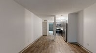 This single-floor residence offers a clean, modern aesthetic throughout its thoughtfully designed layout. The entry opens into a bright living area finished with durable wood-look flooring and neutral white walls, with a window that draws in natural light and creates a welcoming atmosphere.

The kitchen is a standout feature, showcasing dark gray shaker-style cabinetry paired with crisp white countertops and a stylish mosaic tile backsplash in muted tones of gray and white. Stainless steel appliances — including a refrigerator, range, and over-the-range microwave — complete the modern look. A pendant light fixture adds a polished finishing touch above the space.

The open flow between the kitchen and living areas creates a practical and connected layout, with a structural column defining the transition between zones. Wood-look flooring extends throughout the common areas, lending visual continuity and ease of maintenance.

The bedrooms are carpeted for comfort, with neutral tones and clean white walls. The primary bedroom is particularly spacious, featuring two large closets side by side and a generous sliding glass door that fills the room with natural light and offers views of surrounding greenery. A second carpeted bedroom provides additional flexibility.

The bathroom is efficiently designed, featuring a full soaking tub with shower combination, wood-look tile flooring, and brushed nickel fixtures. Textured ceilings are present throughout, adding subtle dimension to the overall interior.