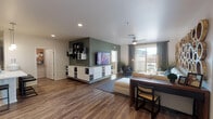 This single-story residence at 8855 N Casa Grande Hwy in Marana, Arizona offers a thoughtfully designed open-concept layout finished with wood-look flooring throughout the main living areas. The living room is a standout space, featuring a ceiling fan, recessed lighting, and a sliding glass door that opens to a private balcony with outdoor views. An accent wall with a built-in media center adds a modern focal point to the room.

The kitchen is well-appointed with dark wood-tone cabinetry, white quartz countertops, a subway tile backsplash, black appliances including a full-size refrigerator and range, and track lighting overhead. A peninsula with bar seating connects the kitchen to the living and dining areas, creating a seamless flow. In-unit washer and dryer hookups are conveniently located nearby.

The bedroom is carpeted for comfort and includes a ceiling fan, a window allowing natural light, and access to a generously sized walk-in closet with built-in shelving and hanging rods. The bathroom features dark vanity cabinetry, a white countertop, a large mirror, and a glass-enclosed shower, all finished with wood-look flooring for a cohesive aesthetic throughout the home.