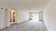 Located at 129–137 Shady Lane Apartments in Schenectady, NY, this single-floor residence offers a thoughtfully designed layout with comfortable living spaces throughout. The open living room is generously sized, featuring plush wall-to-wall carpeting, a textured ceiling, and a sliding glass door with vertical blinds that allows natural light to fill the space and provides views of the surrounding outdoors. A second carpeted room with a wide window and baseboard heating offers flexibility as a bedroom or additional living area, complete with its own wall-mounted thermostat. The kitchen is well-appointed with warm wood cabinetry, white countertops, stainless steel appliances including an electric range and dishwasher, a double sink, and durable tile flooring. Ample upper and lower cabinet storage runs along both sides of the galley-style kitchen, with a view leading directly to the bathroom. The bedroom includes a spacious walk-in closet with built-in shelving and a wall-mounted air conditioning unit for personalized comfort. The bathroom is clean and functional, featuring a full soaking tub and shower combination. Throughout the unit, neutral tones and practical finishes create a bright, move-in-ready environment.