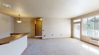 Located at 215 S Conklin Rd in Spokane Valley, WA, this one-bedroom, one-bathroom unit offers a well-organized, single-level layout designed for comfortable everyday living. The open-concept kitchen and living area forms the heart of the home, featuring light maple cabinetry, a peninsula with a dark countertop, black appliances including a refrigerator and range, and tile flooring that transitions seamlessly into plush carpeting in the living space. The living area is generously sized with neutral wall tones, a textured ceiling, and large windows paired with a glass door that invite abundant natural light and offer views of the surrounding neighborhood. The bedroom is a comfortable, well-proportioned retreat with soft carpet, a window with blinds, a baseboard heater, and ample wall space. The bathroom includes a single-sink vanity with warm wood cabinetry, a large mirror with lighted fixture, a tiled floor, and a shower/tub combination. A dedicated closet provides practical storage. Warm-toned wood trim and neutral paint tones throughout create a cohesive and inviting ambiance, making this a functional and move-in-ready space in Spokane Valley.