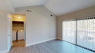 This well-designed single-floor residence offers a thoughtful layout that balances comfort and functionality. The open-concept living and dining area immediately impresses with soaring vaulted ceilings that lend a sense of spaciousness and airiness. A classic fireplace serves as the focal point of the living room, while a large sliding glass door floods the space with natural light and provides direct access to a private balcony with outdoor views of surrounding greenery.

The kitchen is efficiently laid out in an L-shape configuration, featuring white cabinetry, a warm-toned countertop, a double-basin sink, and a full suite of white appliances including a gas range, built-in microwave, dishwasher, and refrigerator. A raised breakfast bar separates the kitchen from the main living area, creating a natural transition between spaces. Light wood-tone flooring runs throughout the main living areas, adding a clean and cohesive aesthetic.

The bedroom is generously proportioned with plush carpeting, vaulted ceilings, and its own sliding glass door opening to an additional outdoor space. A dedicated laundry area is conveniently accessible from the bedroom. The full bathroom is outfitted with a single-sink vanity featuring matching countertops, a large mirror with overhead lighting, and a combined tub and shower enclosure. The overall ambiance is bright, neutral, and move-in ready.