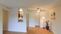 Located at 1701 Lee Rd. in Winter Park, Florida, this single-story residence offers a clean, functional layout designed for comfortable everyday living. The main living area is bright and open, featuring warm-toned hardwood flooring that flows seamlessly throughout the space, contributing to a cohesive and inviting atmosphere. A ceiling fan with a built-in light fixture is centrally positioned overhead, providing both air circulation and ambient lighting.

A defining architectural feature of this home is the pass-through window connecting the living area to the kitchen, creating an open, communicative feel between the two spaces. The kitchen is equipped with warm wood cabinetry, a granite-style countertop at the pass-through, and a full suite of appliances including a refrigerator and range. A separate pantry or storage closet is visible adjacent to the kitchen, offering practical organizational space.

The neutral, light-toned walls throughout the living area create a versatile backdrop that accommodates a variety of décor styles. Doorways lead to additional areas of the home, suggesting a well-connected floor plan. The overall ambiance is warm, approachable, and move-in ready, making this Winter Park residence a practical and comfortable place to call home.
