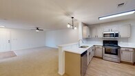This single-story residence is thoughtfully laid out with an open-concept design that connects the kitchen and living areas into one cohesive, generously sized space. The kitchen is well-appointed with raised-panel cabinetry in a neutral taupe finish, white countertops, a tile backsplash, and stainless steel appliances including a range, over-the-range microwave, dishwasher, and a peninsula with an integrated sink. Light wood-look flooring runs throughout the kitchen, transitioning to plush carpet in the living and bedroom areas. A contemporary pendant chandelier illuminates the kitchen peninsula, while a ceiling fan serves the living space.

The living area is open and bright, featuring a front entry with a glass-paneled door and access to natural light. The bedrooms are well-sized, each with carpet flooring, ceiling fans, and windows fitted with blinds that allow abundant natural light. A spacious walk-in closet with wire shelving provides generous storage. The unit includes two bathrooms, both featuring light wood-look flooring, vanities with white countertops, and wall-mounted cabinetry. One bathroom offers a tiled tub-and-shower combination with a classic black accent tile border, while the second features a walk-in shower area. The overall palette is neutral and clean throughout.