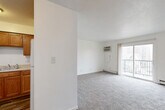 Located at 531 35th St in Des Moines, Iowa, this two-bedroom, one-bathroom unit offers a functional and well-organized single-floor layout. The bright living room features neutral carpet, a textured ceiling, baseboard heating, and a wall-mounted air conditioning unit. A sliding glass door opens to a private balcony, allowing natural light to fill the space and providing outdoor views of the surrounding neighborhood. The kitchen and dining area are combined into one practical space, featuring warm wood-toned cabinetry, a white refrigerator, and hard-surface flooring that transitions seamlessly from the kitchen into the dining zone. Both bedrooms are carpeted and finished with clean white walls, with baseboard heaters providing warmth. The primary bedroom offers a comfortable footprint, while the second bedroom features dual windows with blinds, inviting plentiful natural light. Four closets throughout the unit provide generous storage capacity. The bathroom is finished with wood-look vinyl flooring, a wooden vanity with a white countertop, a wall mirror, and a full tub-shower combination. The overall aesthetic is clean, bright, and neutral, offering a practical living environment in a residential Des Moines neighborhood.