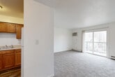 Located at 531 35th St in Des Moines, Iowa, this two-bedroom, one-bathroom unit offers a functional and well-organized single-floor layout. The bright living room features neutral carpet, a textured ceiling, baseboard heating, and a wall-mounted air conditioning unit. A sliding glass door opens to a private balcony, allowing natural light to fill the space and providing outdoor views of the surrounding neighborhood. The kitchen and dining area are combined into one practical space, featuring warm wood-toned cabinetry, a white refrigerator, and hard-surface flooring that transitions seamlessly from the kitchen into the dining zone. Both bedrooms are carpeted and finished with clean white walls, with baseboard heaters providing warmth. The primary bedroom offers a comfortable footprint, while the second bedroom features dual windows with blinds, inviting plentiful natural light. Four closets throughout the unit provide generous storage capacity. The bathroom is finished with wood-look vinyl flooring, a wooden vanity with a white countertop, a wall mirror, and a full tub-shower combination. The overall aesthetic is clean, bright, and neutral, offering a practical living environment in a residential Des Moines neighborhood.