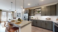 This single-floor residence is designed with a modern aesthetic and a thoughtfully open layout. The kitchen serves as a central feature, outfitted with dark gray shaker-style cabinetry, granite countertops, a white subway tile backsplash, and a full suite of stainless steel appliances. A kitchen island with a granite surface and bar seating anchors the space, illuminated by a trio of stylish pendant lights. Open shelving adds both functionality and visual interest alongside the upper cabinetry.

Wood-look flooring extends throughout the main living areas, connecting the kitchen seamlessly to the living room, which benefits from large windows dressed with blinds and curtain panels that allow ample natural light. Recessed lighting and a ceiling fan contribute to the well-lit, comfortable atmosphere throughout.

The bedroom is carpeted and generously sized, featuring large windows that frame outdoor views and invite natural light. A ceiling fan adds comfort, while the room offers a quiet, well-proportioned retreat. A vanity nook adjacent to the bedroom provides additional functional space.

The bathroom includes a tub-shower combination, a granite-topped vanity with dark cabinetry matching the kitchen, and wood-look flooring. A walk-in closet is accessible directly from the bathroom, offering practical storage.