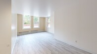 Located at 420 Sherman St SW in Olympia, Washington, this one-bedroom, two-bathroom unit offers a practical and well-organized layout on a single floor. The open-plan kitchen and living area serves as the heart of the home, featuring light wood-style flooring, warm honey-toned cabinetry, and black appliances including a refrigerator, range, and microwave. A circular track lighting fixture illuminates the space, adding a functional design touch. Large double-hung windows in the living area allow generous natural light to flow in, offering views of the surrounding brick exterior and greenery. Baseboard heating runs along the perimeter of the main living spaces, ensuring year-round comfort. The bedroom is carpeted and includes a built-in closet with shelving and sliding doors, providing useful storage. A second closet adds further organizational flexibility. The bathroom features tiled walls in a classic style with a full tub-shower combination. Neutral wall tones and clean white trim throughout the unit contribute to a bright, cohesive aesthetic. The space is thoughtfully laid out to maximize functionality, making efficient use of every square foot in this compact yet complete Olympia residence.