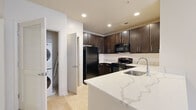 This single-floor residence offers a thoughtfully designed layout with functional living spaces throughout. The kitchen serves as a central highlight, featuring rich dark-espresso cabinetry extending to the ceiling for ample storage, white quartz countertops with subtle veining, and a white subway tile backsplash. Black appliances, including a refrigerator, range, built-in microwave, and dishwasher, complete the space. A peninsula with an undermount sink and additional seating potential connects the kitchen to the open living area, which benefits from recessed and track lighting.

An in-unit laundry closet with a stacked washer and dryer is conveniently positioned near the kitchen. The bedrooms are carpeted and receive generous natural light through large windows overlooking surrounding greenery and brick architecture, each room equipped with a ceiling fan. The primary bedroom includes a walk-in closet with built-in shelving.

Both bathrooms are finished with neutral tile flooring and dark vanity cabinetry topped with white countertops. One bathroom features a shower-tub combination, while the other functions as a powder-style bath. Throughout, the neutral color palette and clean lines create a cohesive, modern aesthetic.
