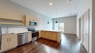 This thoughtfully designed single-floor space offers a seamless blend of modern aesthetics and functional living. The heart of the home is the open-concept kitchen, which flows effortlessly into the living area. The kitchen is outfitted with light maple cabinetry, a classic white subway tile backsplash, stainless steel appliances including a refrigerator with ice maker, electric range, built-in microwave, and dishwasher. A peninsula with a crisp white countertop provides additional prep space and serves as a natural divider between the kitchen and the open living area. Stylish matte black pendant lights hang above, adding a contemporary touch. Rich, dark hardwood flooring runs throughout the main living areas, grounding the space with warmth and continuity. The bedroom is a bright and airy retreat, featuring wood-look flooring and a window dressed with horizontal blinds that allow natural light to filter in while maintaining privacy. The bathroom is finished with floor-to-ceiling white subway tile surrounding a soaking tub and shower combination, lending a clean, timeless look. Neutral wall tones throughout the space enhance the sense of openness and create a calm, inviting ambiance well-suited for modern living.