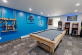 Located at 50 Goldthwaite Rd in Worcester, MA, the Green Hill Park Game Room is a purpose-built recreational facility designed to deliver a well-rounded entertainment experience. The single-room space is thoughtfully laid out to maximize usability, centered around a full-size pool table with a light wood frame and slate-gray felt surface that commands the middle of the room. A wall-mounted cue rack and dedicated billiards signage reinforce the room's identity as a serious gaming destination.

One wall features a bold blue accent, adding energy and visual personality to the space, while the remaining walls are finished in neutral gray, keeping the overall aesthetic clean and modern. Recessed lighting throughout ensures consistent, even illumination. Durable patterned carpet tiles cover the floor, offering both comfort and a practical surface for heavy foot traffic.

Along one side of the room, a collection of classic arcade cabinets is arranged beneath a glowing "Green Hill Park Arcade" sign, accompanied by bar stools for casual play. A dartboard with a rustic wood backing adds another layer of entertainment variety. A high-top bar counter with seating provides a social gathering spot, while a large Connect Four board offers additional recreational options. Multiple windows along one wall allow natural light to filter in, and a glass-paneled door provides convenient access to the exterior.