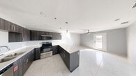 This well-designed 1-bedroom, 1-bathroom unit offers a thoughtfully organized single-floor layout that maximizes every square foot. The open-concept living, dining, and kitchen area serves as the heart of the home, unified by striking marble-look porcelain tile flooring that flows seamlessly throughout. The kitchen is a standout feature, showcasing dark wood-grain cabinetry, bright white quartz countertops, a peninsula island with additional prep space, and a full suite of stainless steel appliances including a range, microwave, dishwasher, and refrigerator. Pendant lighting above the island adds a modern, polished touch. The living area benefits from natural light and features a ceiling fan, with direct access to a private balcony. The bedroom is a comfortable retreat with soft gray walls, a ceiling fan, a dedicated closet, and a window that invites natural light. The bathroom continues the marble-look tile aesthetic with a clean, modern design. A dedicated laundry area with stacked units adds everyday convenience. Neutral gray tones, white trim, and contemporary finishes throughout give this unit a cohesive, modern ambiance.