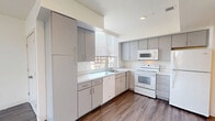 Located at 1781 Massachusetts Ave in Cambridge, MA, this two-bedroom, one-bathroom residence offers a thoughtfully designed single-floor layout with a clean, modern aesthetic throughout. Hardwood-style flooring in a cool gray tone runs continuously through the living areas and bedrooms, creating a cohesive and contemporary feel.

The open kitchen is outfitted with gray cabinetry, white appliances including an electric range, microwave, and dishwasher, and a double-basin sink positioned beneath a window that frames views of the Cambridge streetscape. Ample counter space and abundant cabinet storage make this kitchen highly functional.

The spacious living room benefits from a generous bank of windows on two walls, flooding the space with natural light and offering elevated views of the surrounding neighborhood's brick architecture and tree canopy. A closet is conveniently accessible from the living area.

Both bedrooms feature the same hardwood-style flooring and large windows that bring in plentiful daylight. The primary bedroom includes a double-door closet, while the second bedroom offers a bright, versatile layout.

The bathroom is finished with distinctive navy hexagonal tile flooring, a vanity with mirror, and a clean, efficient design. Overall, this residence presents a bright, well-appointed space in a prime Cambridge location.