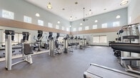 Located at 345 Buckland Hills Drive in Manchester, Connecticut, this fitness center offers a comprehensive workout facility designed to support a full range of exercise routines. The space is housed on a single floor and is distinguished by its soaring ceilings, which lend an open, airy atmosphere to the room. Rows of clerestory windows positioned near the top of the walls allow abundant natural light to fill the space throughout the day.

The facility is outfitted with an extensive selection of cardio equipment, including elliptical machines, treadmills, and stationary bikes, arranged to maximize floor space and ease of movement. A dedicated strength training area features a variety of cable machines and weight stations, complemented by a well-stocked dumbbell rack with a flat bench for free weight exercises. Full-length mirrors line portions of the walls, enhancing the sense of space and providing users with proper form feedback during workouts.

Durable rubber flooring covers the entire workout area, offering safety and comfort underfoot. Pendant lighting hangs from the high ceiling alongside a ceiling fan, ensuring the space remains well-lit and ventilated. Hygiene stations equipped with Purell sanitizing wipes and waste receptacles are conveniently positioned throughout the room. A mounted flat-screen television adds an entertainment element to the cardio area, rounding out this fully functional and thoughtfully maintained fitness facility.