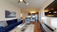 This single-floor residence offers a thoughtfully designed open-concept layout that seamlessly connects the living, dining, and kitchen areas. The living room features rich hardwood flooring, a ceiling fan with integrated lighting, recessed lighting, and large windows fitted with blinds that invite natural light throughout the day. A tufted navy sofa and accent chairs anchor the comfortable seating area.

The kitchen is a standout feature, boasting rich dark-wood cabinetry, granite countertops, a classic subway tile backsplash, and a full suite of stainless steel appliances including a gas range, microwave, and refrigerator. A large granite-topped island with bar seating serves as both a functional workspace and a casual dining area, illuminated by elegant pendant lights.

The residence includes two bedrooms, each carpeted and filled with natural light from generously sized windows. The primary bedroom benefits from access to a spacious walk-in closet outfitted with wire shelving and hanging rods for ample storage. The full bathroom features warm wood cabinetry, a granite vanity top, and tile flooring with a clean, neutral palette.

A dedicated in-unit laundry room with side-by-side washer and dryer and overhead shelving adds everyday convenience to this well-rounded home.