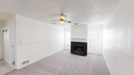 This single-floor residence offers a well-organized layout with a bright, neutral interior throughout. The spacious living room serves as the heart of the home, featuring plush carpet flooring, a ceiling fan with light fixture, a textured ceiling, and a striking black tile fireplace with a white mantel. Multiple windows flood the room with natural light, creating an open and airy atmosphere. The living area flows seamlessly toward the kitchen, which is equipped with white cabinetry, light laminate flooring, black appliances including a refrigerator and range, and a mirrored sliding door that adds depth to the space. A peninsula counter separates the kitchen from the living area, offering a functional transition between the two spaces. The bedrooms are carpeted and generously sized, each featuring mirrored sliding closet doors that enhance the sense of space. One bedroom includes an arched window that brings in additional natural light. The bathroom is clean and functional, with a tub-shower combination, a vanity with white cabinetry, and light wood-style flooring that complements the overall aesthetic. Throughout the home, the consistent use of white walls, neutral tones, and natural light creates a cohesive and inviting environment.