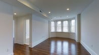Located in the heart of Philadelphia's vibrant Center City neighborhood, this single-floor residence on Locust Street combines classic architectural character with modern, clean-lined finishes. The living area immediately impresses with its rich, dark hardwood floors that reflect the abundant natural light pouring in through a graceful curved bay window — a distinctive architectural feature that frames views of the surrounding cityscape. Recessed lighting throughout the ceiling provides even, warm illumination, complementing the natural light from the bay's multiple double-hung windows dressed with clean white blinds. The walls are finished in a crisp, neutral white palette, enhancing the sense of openness and allowing the warm tones of the hardwood to take center stage. Substantial white baseboards and clean door casings add a refined, traditional touch to the space. A doorway visible from the main living area leads to an additional room, suggesting a versatile layout suited for a variety of living arrangements. Overall, the space strikes a balance between timeless urban elegance and functional, well-maintained interiors, making it an inviting residence in one of Philadelphia's most sought-after addresses.