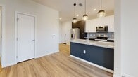 This well-appointed one-bedroom, one-bathroom residence in Northglenn, Colorado offers a thoughtfully designed open-concept layout with modern finishes throughout. Light wood-look flooring flows seamlessly across the main living areas, creating a bright and cohesive feel. The kitchen serves as a focal point of the home, showcasing a striking two-tone design with dark navy cabinetry, white upper cabinets, a granite-topped island with pendant lighting, a tile backsplash, and a full suite of stainless steel appliances including a French door refrigerator, range, and over-the-range microwave. The living area is bathed in natural light from multiple large windows and features a ceiling fan for year-round comfort. The spacious primary bedroom is finished with plush carpet, a ceiling fan, and generous windows that bring in ample daylight, with access to multiple closets for excellent storage. The bathroom is elegantly appointed with a double-sink granite vanity, dark cabinetry, backlit mirrors, and a walk-in shower. A dedicated in-unit laundry room houses a full-size washer and dryer with overhead shelving, adding everyday convenience. Clean white walls and crisp trim complete the modern, move-in-ready aesthetic of this Northglenn home.