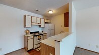 Located at 372 James Way in Marion, Ohio, this single-floor residence offers a practical and comfortable layout designed for everyday living. The kitchen is a standout feature, showcasing white cabinetry that extends to the upper walls, providing generous storage space. A gas range and oven, a full-size refrigerator, and a double-basin sink make this kitchen fully equipped for meal preparation. A peninsula-style breakfast bar with a wood-toned base separates the kitchen from the adjacent living area, offering a casual dining or workspace option. The flooring transitions from warm hardwood in the kitchen to carpet in the neighboring spaces, adding a cozy contrast throughout the home. A textured ceiling and flush-mount ceiling light provide a classic, understated finish to the kitchen area. A pass-through opening adds an architectural touch that enhances the open feel between rooms. The overall ambiance is functional and welcoming, with a neutral color palette of whites and warm wood tones that keeps the space feeling bright and cohesive. This single-story home on James Way presents a straightforward, well-organized living environment suited to a range of occupants.