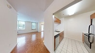 Located at 225 Grand Street in Jersey City's vibrant downtown, Unit 135 is a well-organized studio offering a smart, functional layout across a single floor. The open-plan kitchen and living area form the heart of the unit, where warm parquet flooring creates a cohesive and inviting atmosphere throughout. The kitchen is outfitted with stainless steel appliances — including a refrigerator, range, and microwave — set against rich wood cabinetry and a clean white breakfast bar that doubles as a pass-through and casual dining surface. The living area benefits from large windows that usher in natural light and frame views of the surrounding greenery, contributing to an airy, open feel. A wall-mounted HVAC unit ensures year-round climate control. Closet space is integrated into the living area, providing practical storage solutions. The bathroom features large-format tile flooring, a vanity with mirrored storage, and a clean, neutral palette. Crisp white walls throughout the unit lend a bright, modern character, while the parquet flooring adds warmth and texture. Situated in Jersey City's desirable 07302 zip code, this unit offers convenient access to transportation, dining, and the waterfront.