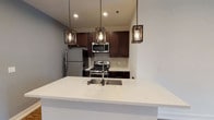 This single-floor residence showcases a thoughtfully designed open-concept layout where the kitchen and living area flow seamlessly together. The kitchen is a standout feature, equipped with dark espresso cabinetry, stainless steel appliances including a gas range, microwave, and refrigerator, complemented by a neutral tile backsplash and a white quartz peninsula with an undermount sink. Three industrial-style pendant lights add character overhead, while recessed lighting provides consistent illumination throughout.

The expansive living area extends toward a sliding glass door framed by a stone accent wall, inviting natural light and outdoor views. Rich wood-look flooring runs throughout the main living spaces and bedrooms, anchoring the contemporary aesthetic.

Multiple bedrooms feature clean white walls, recessed lighting, and generous closet space. Windows in each room bring in natural light and exterior views. Two full bathrooms mirror the kitchen's design language, each offering dark vanity cabinetry, quartz countertops, and a tub/shower combination with white subway tile surround. The overall ambiance is modern, clean, and move-in ready.