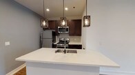 This single-floor residence showcases a thoughtfully designed open-concept layout where the kitchen and living area flow seamlessly together. The kitchen is a standout feature, equipped with dark espresso cabinetry, stainless steel appliances including a gas range, microwave, and refrigerator, complemented by a neutral tile backsplash and a white quartz peninsula with an undermount sink. Three industrial-style pendant lights add character overhead, while recessed lighting provides consistent illumination throughout.

The expansive living area extends toward a sliding glass door framed by a stone accent wall, inviting natural light and outdoor views. Rich wood-look flooring runs throughout the main living spaces and bedrooms, anchoring the contemporary aesthetic.

Multiple bedrooms feature clean white walls, recessed lighting, and generous closet space. Windows in each room bring in natural light and exterior views. Two full bathrooms mirror the kitchen's design language, each offering dark vanity cabinetry, quartz countertops, and a tub/shower combination with white subway tile surround. The overall ambiance is modern, clean, and move-in ready.