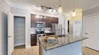 Located at 18110 Laurel Haven Dr in Greenville, SC, this efficient single-floor residence offers a thoughtfully designed layout comprising a kitchen, living room, bedroom, bathroom, and closet. The kitchen serves as a focal point of the home, showcasing rich dark-brown cabinetry, a subway tile backsplash, stainless steel appliances including a range, over-the-range microwave, and refrigerator, and a granite-topped island with a built-in sink and pendant lighting overhead. Track lighting adds a modern touch, while an adjacent open pantry provides convenient storage. The living room features light wood-style flooring, crown molding, a ceiling fan, and a window that invites natural light and outdoor views. The bedroom is carpeted for comfort, includes its own ceiling fan, and benefits from a window overlooking greenery, creating a calm and restful environment. A dedicated closet offers additional storage. The bathroom is clean and functional, appointed with a granite-topped vanity with dark cabinetry, a tub-shower combination, and wood-style flooring that ties the space together. Neutral gray walls throughout the residence create a cohesive and modern aesthetic.