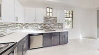 Located in Buckeye, AZ, this two-story, 2-bedroom, 2-bathroom home offers a thoughtfully designed layout spread across two well-proportioned floors. The main level makes an immediate impression with a dramatic double-height living area, soaring ceilings, and large windows that flood the space with natural light. Light-toned luxury vinyl flooring runs throughout the main level, complementing the clean, modern aesthetic. The kitchen is a standout feature, showcasing two-tone cabinetry — dark lower cabinets paired with crisp white uppers — white quartz countertops, a mosaic tile backsplash, and a full suite of stainless steel appliances including a range, microwave, and dishwasher. A sliding glass door on the upper level opens to an outdoor balcony, extending the living space outdoors. The upper floor is home to both bedrooms, connected by a carpeted hallway with a sleek metal railing overlooking the living area below. The spacious primary bedroom includes access to a walk-in closet with built-in shelving. Two full bathrooms serve the home: one features a tub-shower combo with glass sliding doors, while the other offers a walk-in shower with classic black-and-white tile accents and a white vanity. Ceiling fans are present throughout for added comfort.