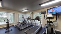 Located at SW Barnes Rd in West Haven, Oregon, this single-story fitness center offers a comprehensive workout environment designed to accommodate a wide range of exercise needs. The space is thoughtfully organized into distinct functional zones, each outfitted with dedicated equipment to support both cardio and strength training routines.

The cardio area is lined with multiple treadmills, elliptical trainers, and a stationary bike, all positioned along large windows that frame lush, tree-lined views of the surrounding Pacific Northwest landscape. Wall-mounted televisions provide additional entertainment during workouts. Overhead fluorescent lighting ensures the space remains consistently well-lit throughout.

The strength training section features a multi-station cable machine, adjustable weight benches, and a well-stocked dumbbell rack spanning a wide range of weights. Stability balls and other functional training accessories are also available. Full-length mirrors line one wall, enhancing the sense of openness and allowing users to monitor their form.

Durable rubber flooring covers the entire space, providing both safety and comfort underfoot. The neutral-toned walls and practical layout create a focused, functional atmosphere suited for daily fitness use.