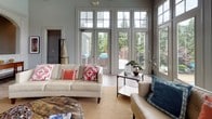 Located at 425 Williams Dr in Marietta, Georgia, this single-floor space showcases a thoughtfully crafted interior that blends classic architectural detail with an open, airy atmosphere. The centerpiece of the space is a dramatic great room highlighted by soaring vaulted ceilings, a ceiling fan, and an expansive wall of floor-to-ceiling windows and French doors that flood the interior with natural light and provide sweeping views of the lush, tree-lined surroundings and adjacent waterfront. Light wood-toned flooring runs throughout, lending warmth and continuity to the open layout. Elegant arched doorways with detailed white millwork frame transitions between rooms, adding a refined architectural character to the space. These arches lead to multiple connected areas, including what appears to be a kitchen with a counter-height bar and additional gathering spaces, each benefiting from the same bright, neutral palette. The living area is generously proportioned, comfortably accommodating multiple seating arrangements centered around a woven area rug. French doors open directly to an outdoor patio, reinforcing the seamless connection between interior and exterior. Overall, the space exudes a welcoming, upscale ambiance defined by architectural elegance, natural light, and gracious proportions.