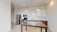 Located at 1295 Chesapeake Ave in Columbus, OH, this thoughtfully designed one-bedroom, one-bathroom unit offers a comfortable and modern living experience across a single floor. The kitchen is a standout feature, showcasing a two-tone cabinetry design with warm wood lower cabinets and crisp white upper cabinets, complemented by a classic white subway tile backsplash and light wood-style flooring. Stainless steel appliances, including a refrigerator, range, and dishwasher, add a contemporary touch, while pendant lighting and a track lighting system illuminate the space efficiently. A kitchen island with a dark countertop provides additional prep and dining space. The bathroom is finished with elegant large-format marble-look tile covering both the floors and walls, creating a cohesive and luxurious aesthetic. An open walk-in shower area adds a clean, modern feel. The bedroom is bright and inviting, with plush wall-to-wall carpeting and multiple windows fitted with blinds that allow generous natural light to fill the room. A dedicated closet provides practical storage. The overall design palette is light and neutral, contributing to an airy, welcoming ambiance throughout the unit.