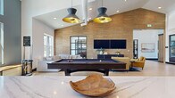 Located in Fort Collins, Colorado, this Game Room & Coworking Lounge is a thoughtfully designed, single-floor amenity space offering a generous footprint for both recreation and productivity. The interior blends modern farmhouse and contemporary design elements, highlighted by soaring vaulted ceilings, light hardwood flooring, shiplap accent walls, and floor-to-ceiling black-framed glass partitions that lend an open, airy aesthetic throughout.

The game room area serves as a social centerpiece, featuring a full-size billiards table beneath striking black-and-gold pendant lights. A textured grasscloth accent wall frames a mounted flat-screen TV and lounge seating, creating an inviting entertainment zone with a plush sectional sofa.

Adjacent to the game room, a well-appointed kitchenette offers sage-green cabinetry, a waterfall quartz island, matte black fixtures, open wood shelving, and stainless appliances — ideal for casual gatherings or extended work sessions.

The coworking lounge provides abundant natural light through oversized windows with outdoor views, high communal tables, window bench seating, and patterned carpet flooring. Multiple enclosed "vault" private offices with black-framed glass doors offer quiet, focused workspaces. The entry foyer features warm wood columns and a skylight, welcoming guests with an elegant yet functional first impression.