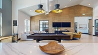 Located in Fort Collins, Colorado, this Game Room & Coworking Lounge is a thoughtfully designed, single-floor amenity space offering a generous footprint for both recreation and productivity. The interior blends modern farmhouse and contemporary design elements, highlighted by soaring vaulted ceilings, light hardwood flooring, shiplap accent walls, and floor-to-ceiling black-framed glass partitions that lend an open, airy aesthetic throughout.

The game room area serves as a social centerpiece, featuring a full-size billiards table beneath striking black-and-gold pendant lights. A textured grasscloth accent wall frames a mounted flat-screen TV and lounge seating, creating an inviting entertainment zone with a plush sectional sofa.

Adjacent to the game room, a well-appointed kitchenette offers sage-green cabinetry, a waterfall quartz island, matte black fixtures, open wood shelving, and stainless appliances — ideal for casual gatherings or extended work sessions.

The coworking lounge provides abundant natural light through oversized windows with outdoor views, high communal tables, window bench seating, and patterned carpet flooring. Multiple enclosed "vault" private offices with black-framed glass doors offer quiet, focused workspaces. The entry foyer features warm wood columns and a skylight, welcoming guests with an elegant yet functional first impression.