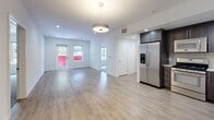 This contemporary single-floor residence showcases a clean, modern aesthetic throughout its thoughtfully designed layout. The open-concept living and dining area features light-toned hardwood-style flooring, recessed lighting, and a pendant light fixture, creating a bright and welcoming atmosphere. Large windows allow natural light to fill the space, with views of surrounding greenery visible from the bedrooms.

The kitchen is outfitted with dark wood cabinetry, white quartz countertops, a subway tile backsplash, and a full suite of stainless steel appliances, including a gas range, built-in microwave, dishwasher, and a French door refrigerator with an in-door ice and water dispenser. Recessed lighting above the workspace adds both functionality and style.

The carpeted bedrooms offer a comfortable retreat, with one featuring a frosted glass sliding closet door providing access to built-in shelving and hanging rods. Another bedroom benefits from a large window framing an outdoor view. A spacious walk-in closet with extensive wire shelving and hanging rails adds generous storage capacity.

The bathrooms are finished with large-format tile flooring, dark wood vanities with undermount sinks, wide mirrors, and glass-enclosed tub-shower combinations, delivering a polished, spa-like experience throughout.