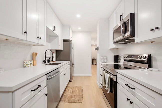 Sleek kitchen with stainless steel appliances, white cabinets, and open layout. - 1013 S Sunshine Ave