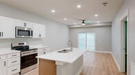 Located at 8801 Mohave Dr in Lincoln, Nebraska, this thoughtfully designed one-bedroom, one-bathroom unit offers a clean, contemporary aesthetic throughout its efficiently organized single floor. The open-concept kitchen and living area serves as the heart of the home, anchored by a central island with a white quartz countertop and undermount sink. Crisp white shaker cabinets with matte black hardware complement a full suite of stainless steel appliances, including a French door refrigerator, electric range, and over-the-range microwave. Light hardwood-style flooring flows throughout the main living areas, enhancing the bright, airy feel. The living area benefits from recessed lighting, a ceiling fan, and sliding glass doors that open to a private balcony, inviting natural light and outdoor views. The spacious primary bedroom features plush carpet, recessed lighting, and access to generous closet storage with built-in shelving. A dedicated laundry closet with a full-size washer and dryer adds everyday convenience. Neutral gray tones on the walls throughout create a calm, cohesive palette, making this well-appointed unit an inviting and functional place to call home.